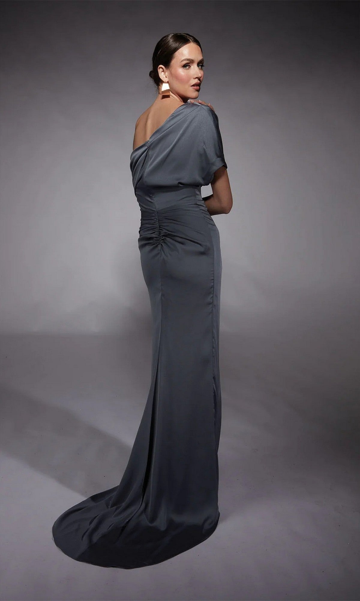 A woman poses in the Alyce 27748 long formal dress, featuring a fitted slate gray satin design with off-the-shoulder sleeves, ruched bodice, and slight train, set against a plain studio backdrop.